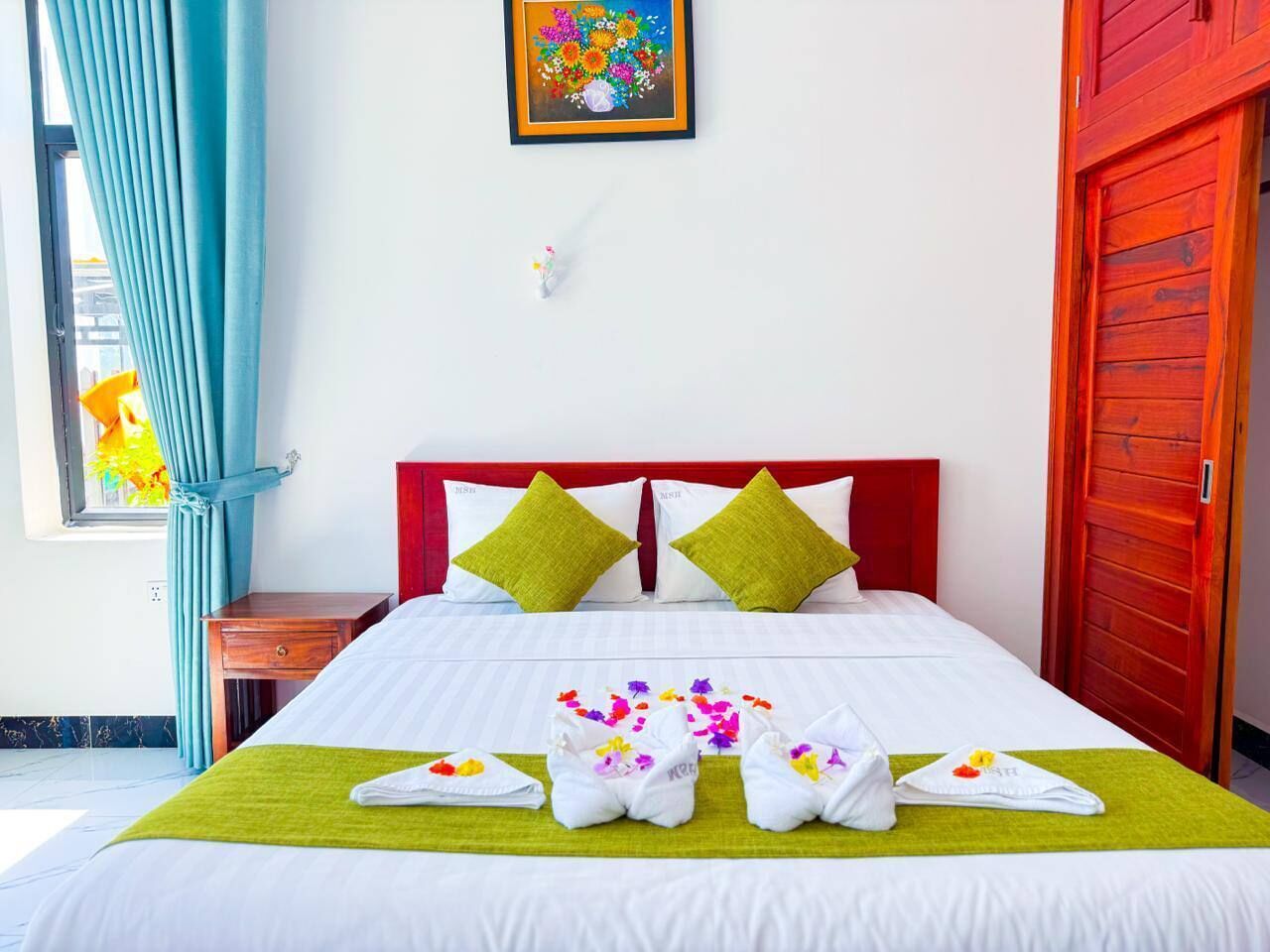 Une chambre d’hôtel avec un lit, une tête de lit rouge, un plaid vert et un tableau accroché au mur.