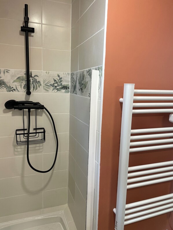 A bathroom with a shower, a towel rack, and a tiled wall with a leaf pattern.