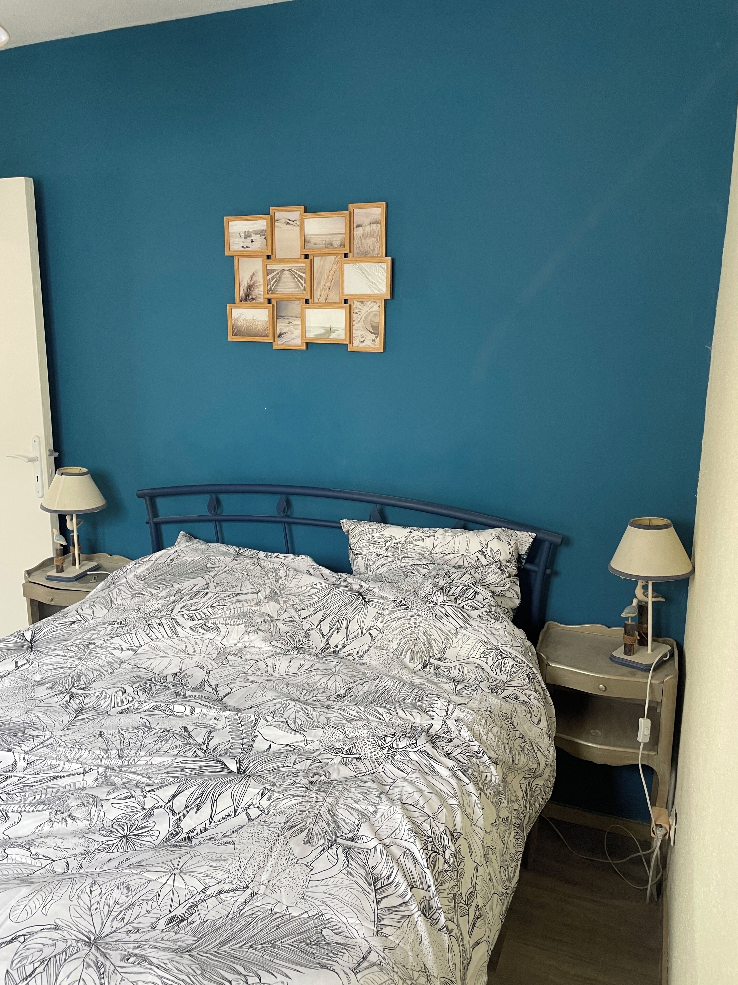 A bedroom with a bed, two bedside tables, a wall-mounted picture frame, and a lamp on each table.