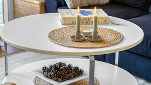 Una mesa redonda blanca con dos velas y un libro titulado 'DANSKE DOMMERFUE' sobre un camino de mesa tejido.