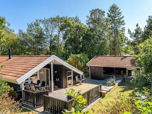 Eine zweistöckige Holzhütte mit einer Terrasse, umgeben von einem Wald.