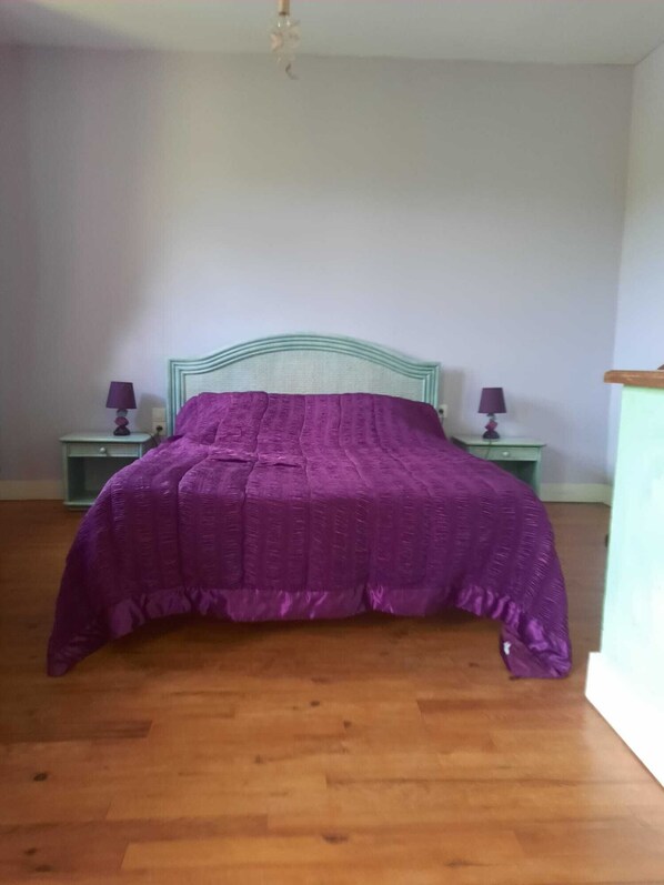 A bedroom with a bed, two nightstands, and a wooden floor.