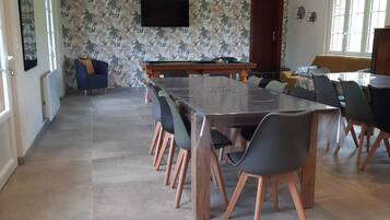 Un comedor amplio con una mesa larga, múltiples sillas y un televisor montado en la pared.