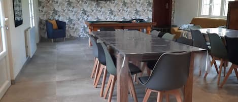 A spacious dining area with a long table, multiple chairs, and a television mounted on the wall.
