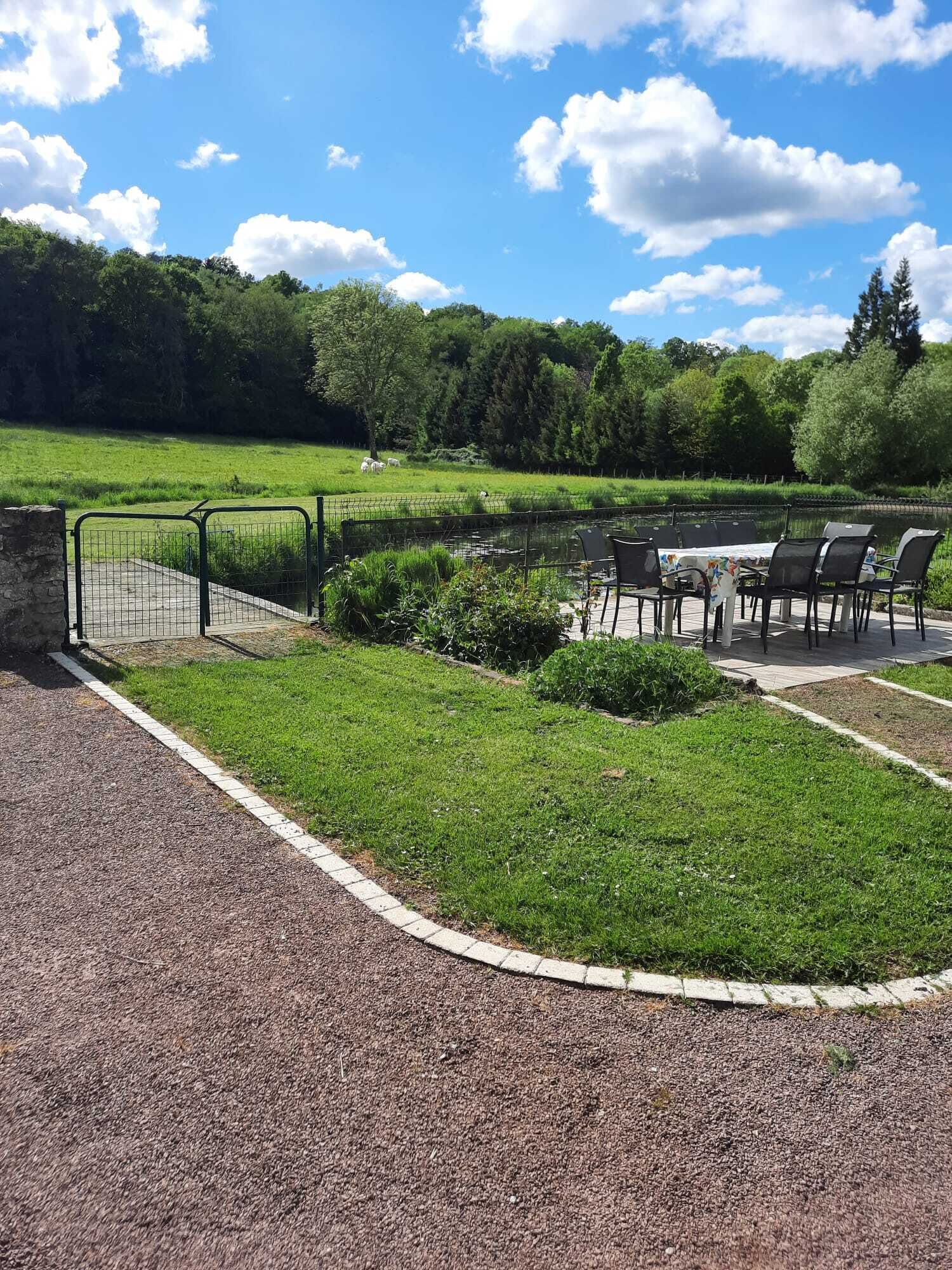 Un parque con un sendero pavimentado, un área verde y una zona de estar con mesas y sillas.