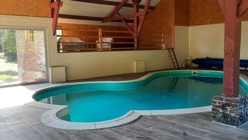 Una piscina interior con una cubierta de madera, un muro de ladrillo y vistas al exterior.