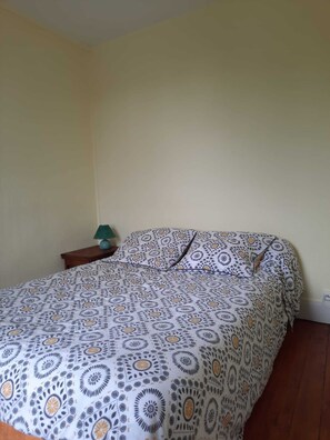 A bed with a patterned bedspread, a bedside table with a lamp, and a wall socket.