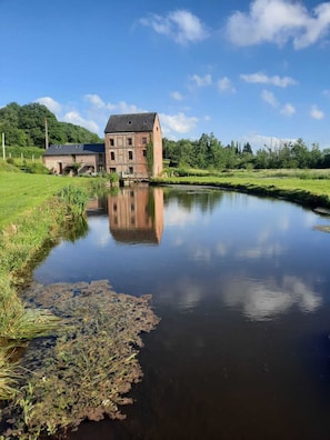 A riverside view with a large brick building and a smaller structure in the background.