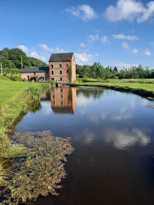 A riverside view with a large brick building and a smaller structure in the background.