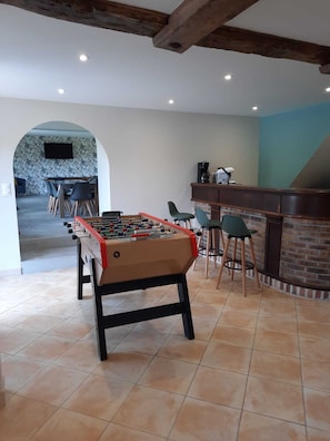 A foosball table in a room with a kitchen area, bar stools, and a fireplace.