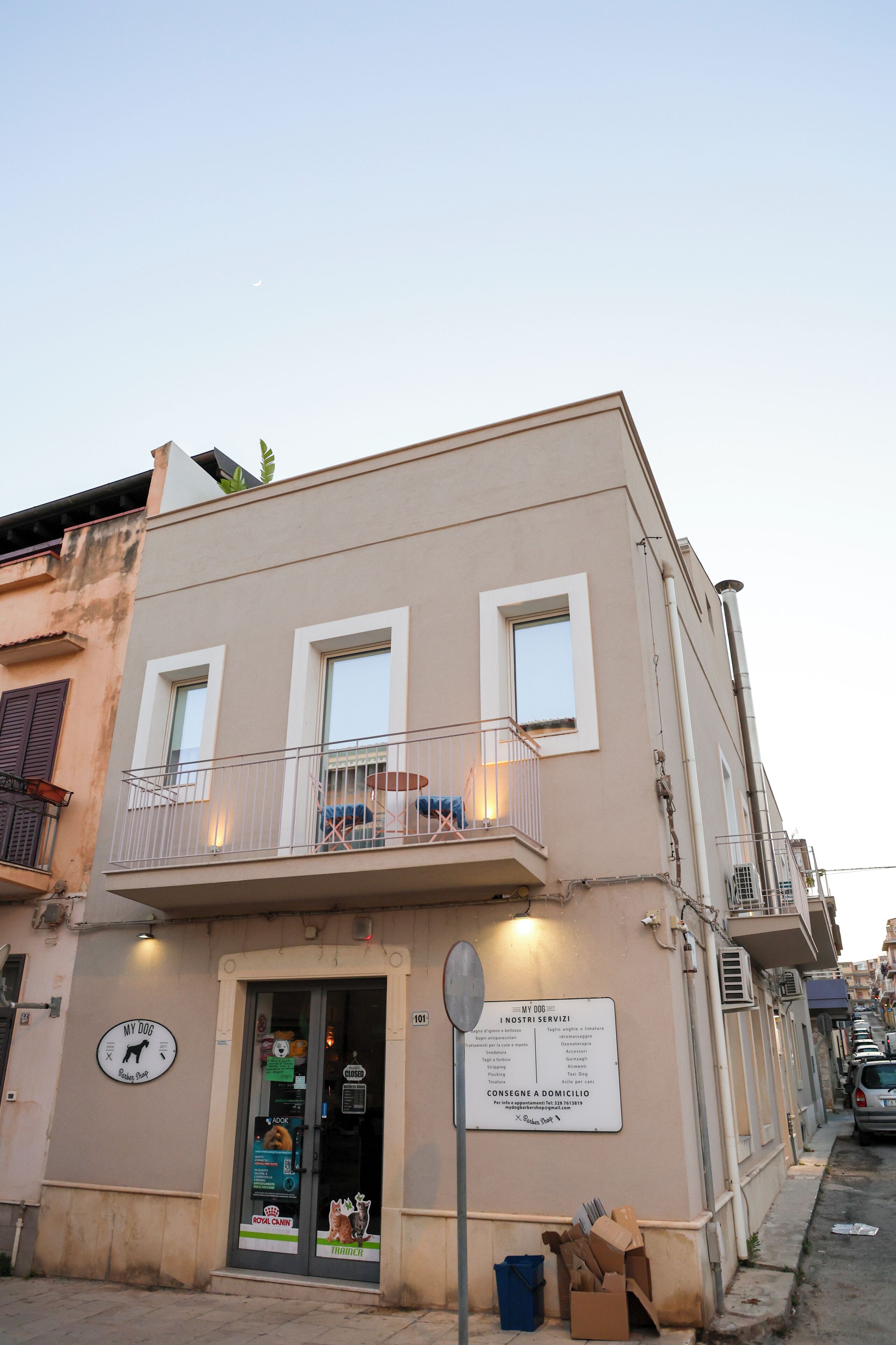 A building with a ground-floor shop, a balcony with a railing, and a signboard with text.
