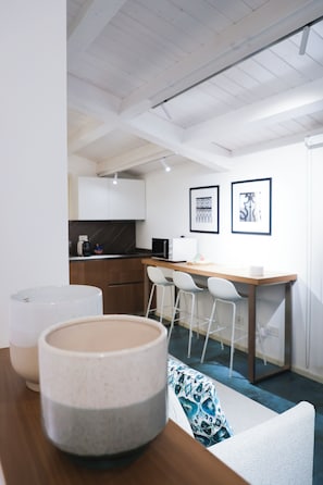 A modern kitchen with white cabinets, a wooden countertop, and a bar area with white chairs. There are two framed pictures on the wall.