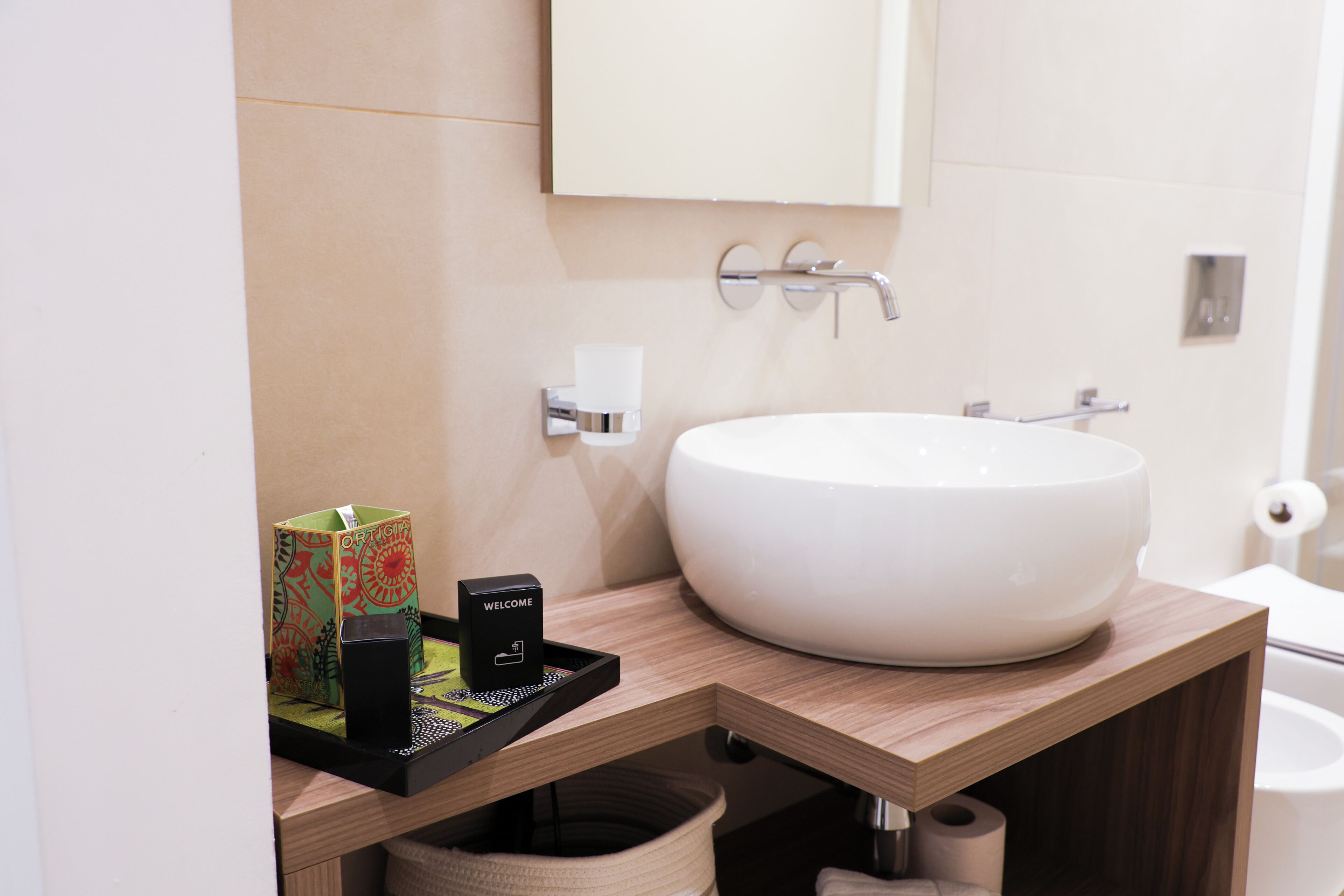 A modern bathroom with a large white sink, a mirror above it, and a toilet visible in the background.