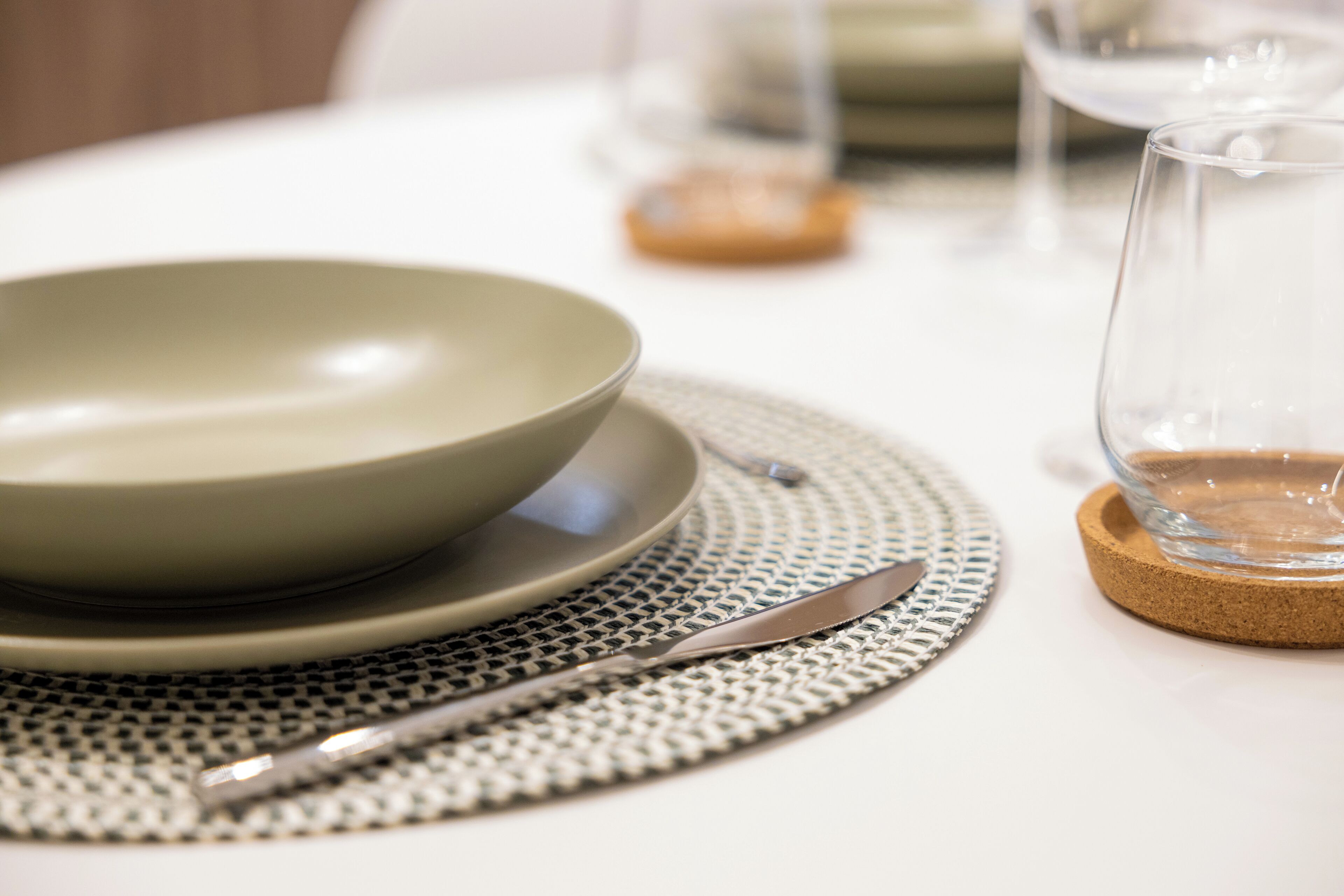 A table with a bowl, a knife, and a glass on a cork coaster.