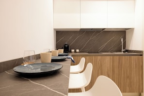 A modern kitchen with a marble backsplash, a built-in stove, and a sink. There are two white chairs and a blue plate on the counter. - Dimora Zahira Your Italian Escape (Marina di Ragusa)