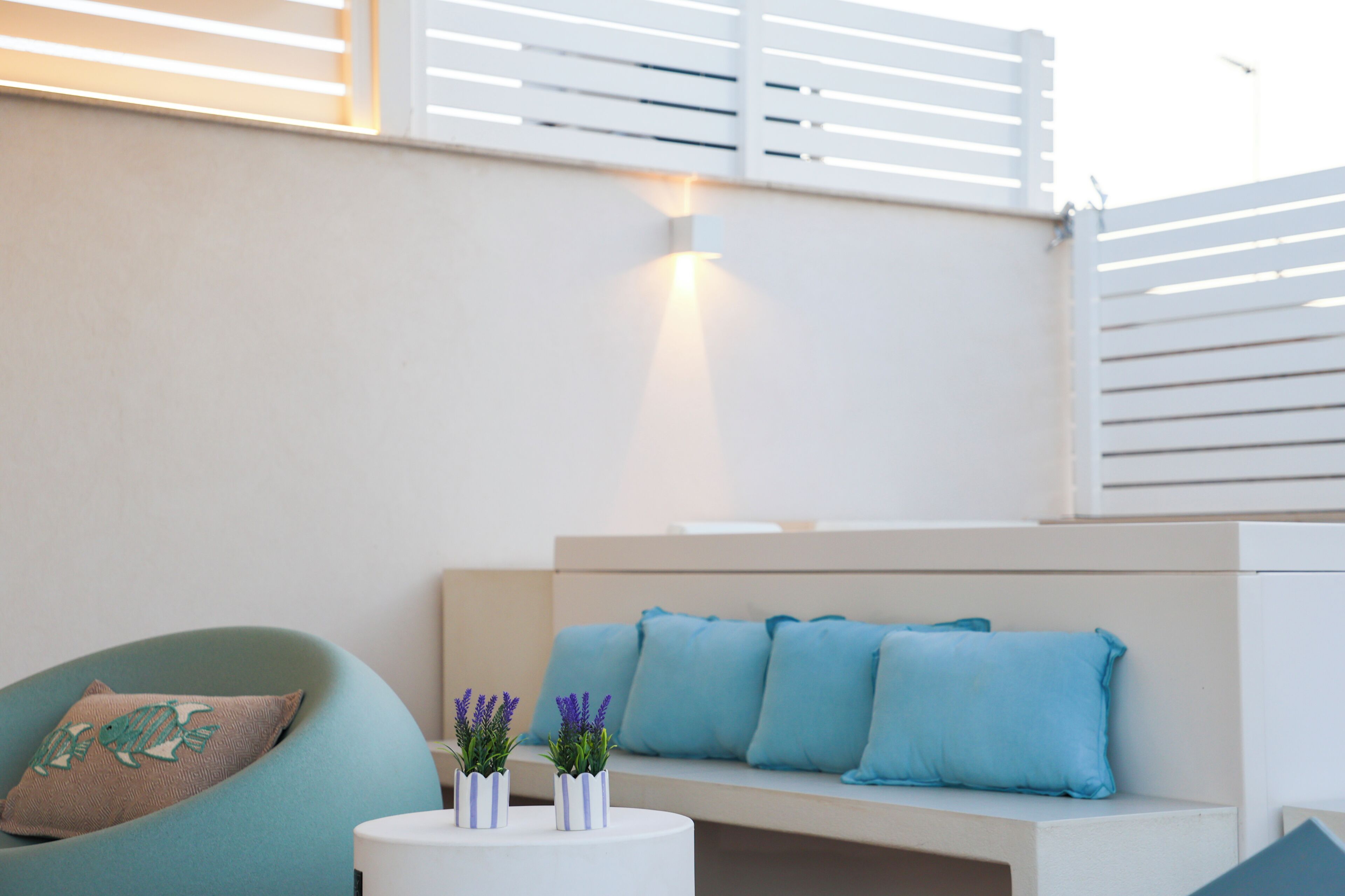 A modern living area with a sofa, cushions, a round table with decorative items, and a wall-mounted light.