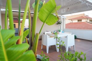 Una terraza con una mesa y sillas blancas, rodeada de plantas en macetas.