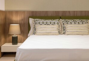 Una cama bien tendida con un cabecero verde, una lámpara de noche y almohadones estampados.