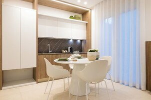 Una cocina moderna con armarios blancos, salpicadero de mármol y una zona de comedor con una mesa redonda y sillas blancas.