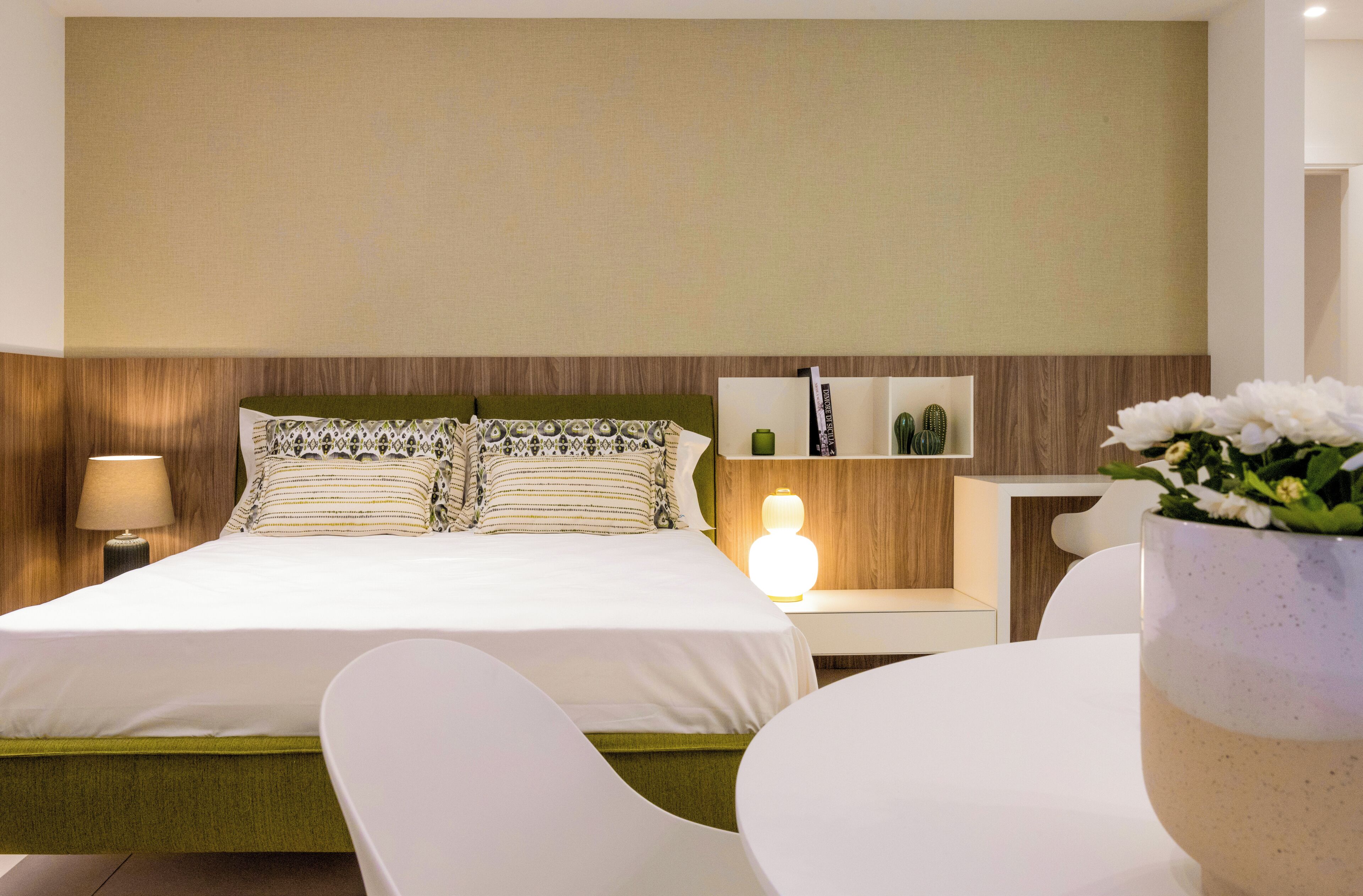 Een hotelkamer met een bed, nachtkastjes, een lamp, een stoel en een vaas met bloemen.