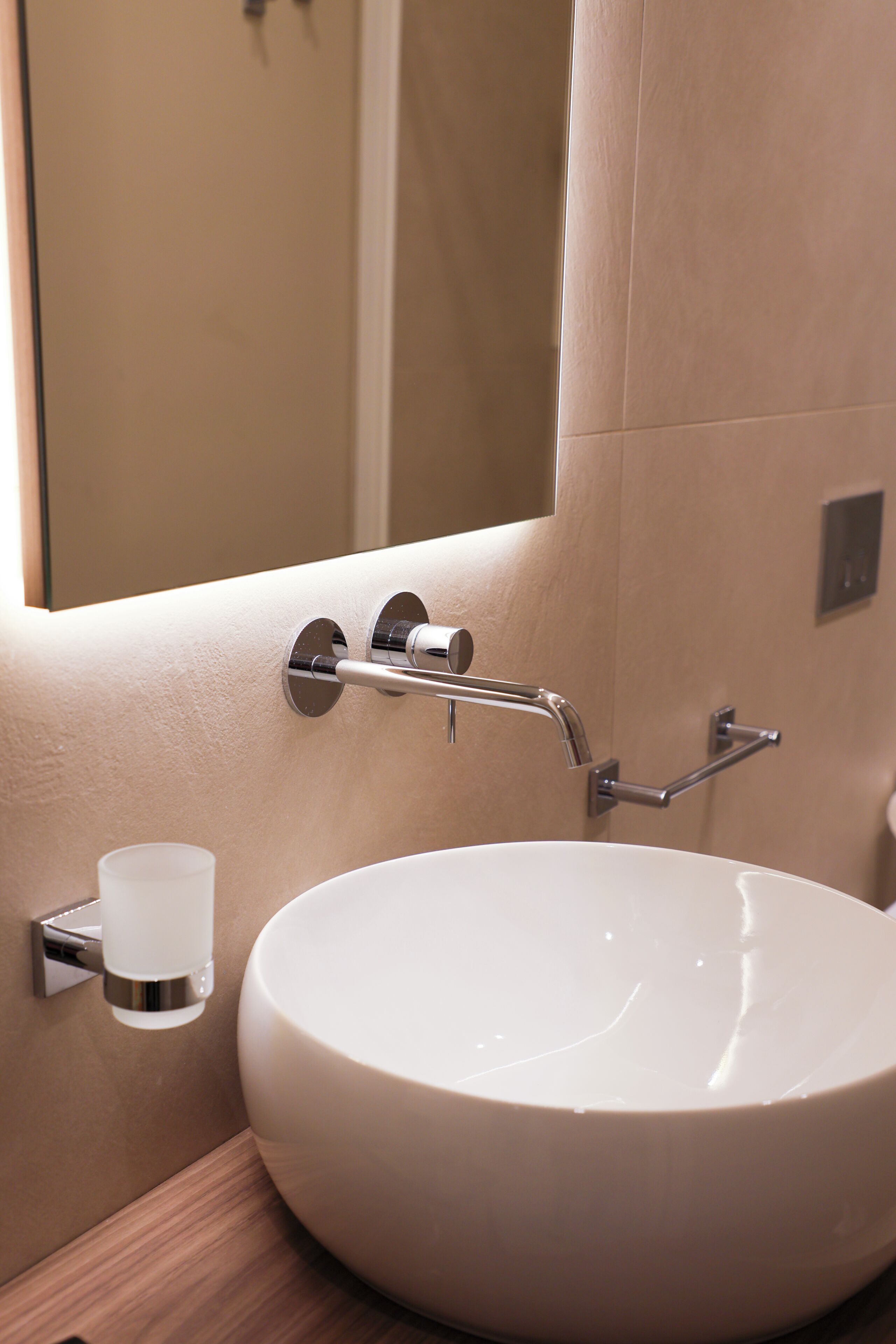 Une salle de bain avec un lavabo rond blanc, un robinet chromé et un petit porte-gobelet.