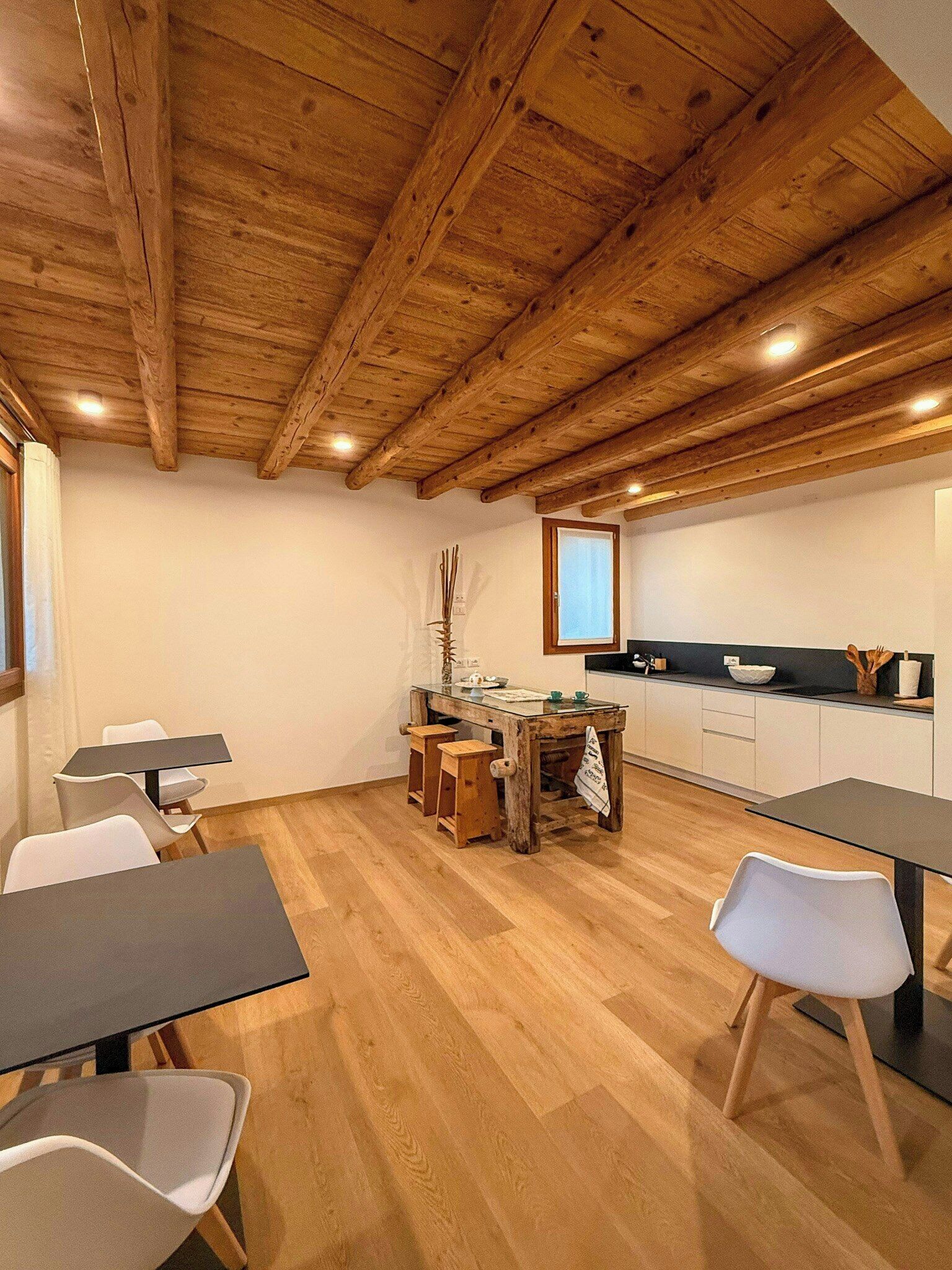 Un espace repas avec un plafond en bois, une table en verre et des chaises blanches.
