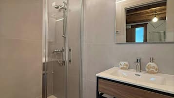 Un bagno moderno con doccia vetrata, soffitto in legno e un mobile lavabo con specchio e due erogatori di sapone.