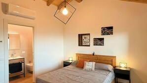 A bedroom with a wooden bed, bedside tables, a hanging light fixture, and a bathroom visible through an open door.
