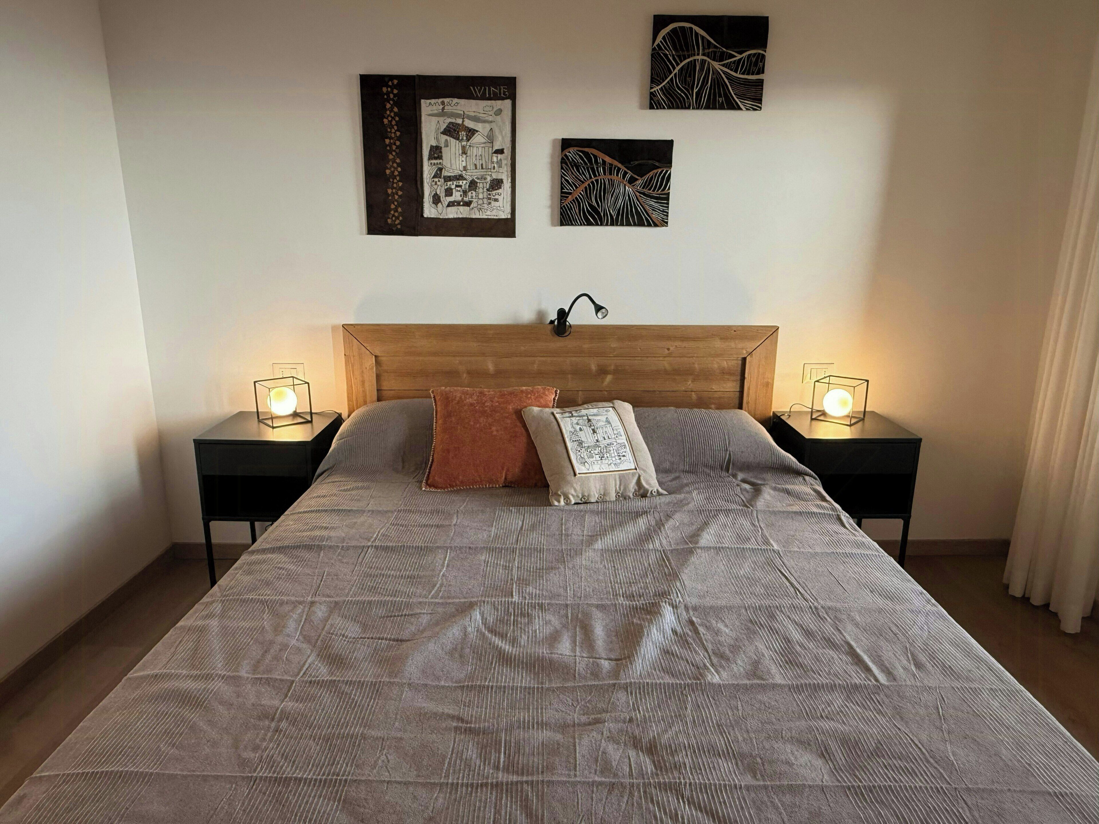 Un letto con testiera in legno, due comodini con lampade e due opere d'arte appese al muro.