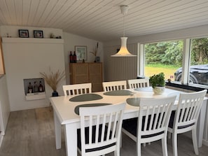 Ein Essbereich mit weißem Tisch und Stühlen, einer Hängelampe und Blick ins Freie.
