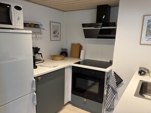 Eine kleine Küche mit Kühlschrank, Kaffeemaschine, Backofen und Mikrowelle.