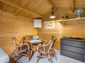 Puisesti sisustettu tila, jossa on pyöreä pöytä ja punotut tuolit, pieni kaappi ja seinälle asennettu tuuletin.