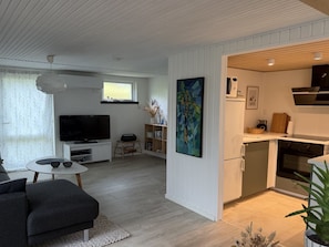 Ein modernes Wohnzimmer mit Flachbildfernseher, einer Couch und einer Essecke mit Tisch und Stühlen.