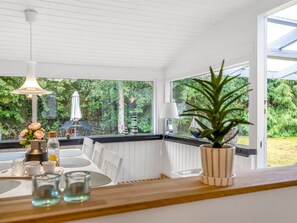 A dining area with a table set for two, a potted plant, and a view of greenery outside.