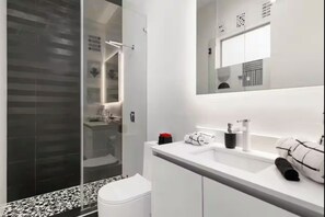 Un bagno moderno con box doccia in vetro, un lavandino bianco con specchio e un water.