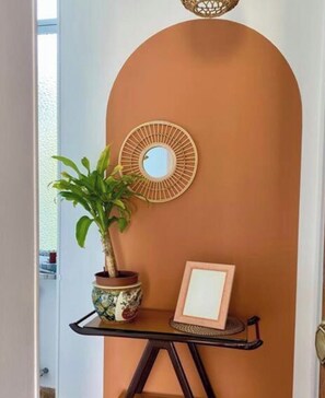 Ein Zimmer mit einer gewölbten Wand, einer Topfpflanze, einem Spiegel und einem kleinen Tisch mit einem Bilderrahmen.