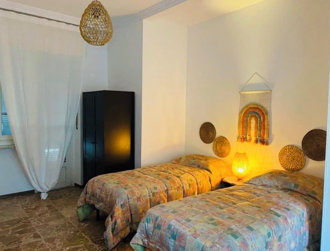 A room with two beds, a wardrobe, a hanging light fixture, and a wall decoration.