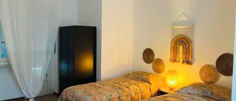 A room with two beds, a wardrobe, a hanging light fixture, and a wall decoration.