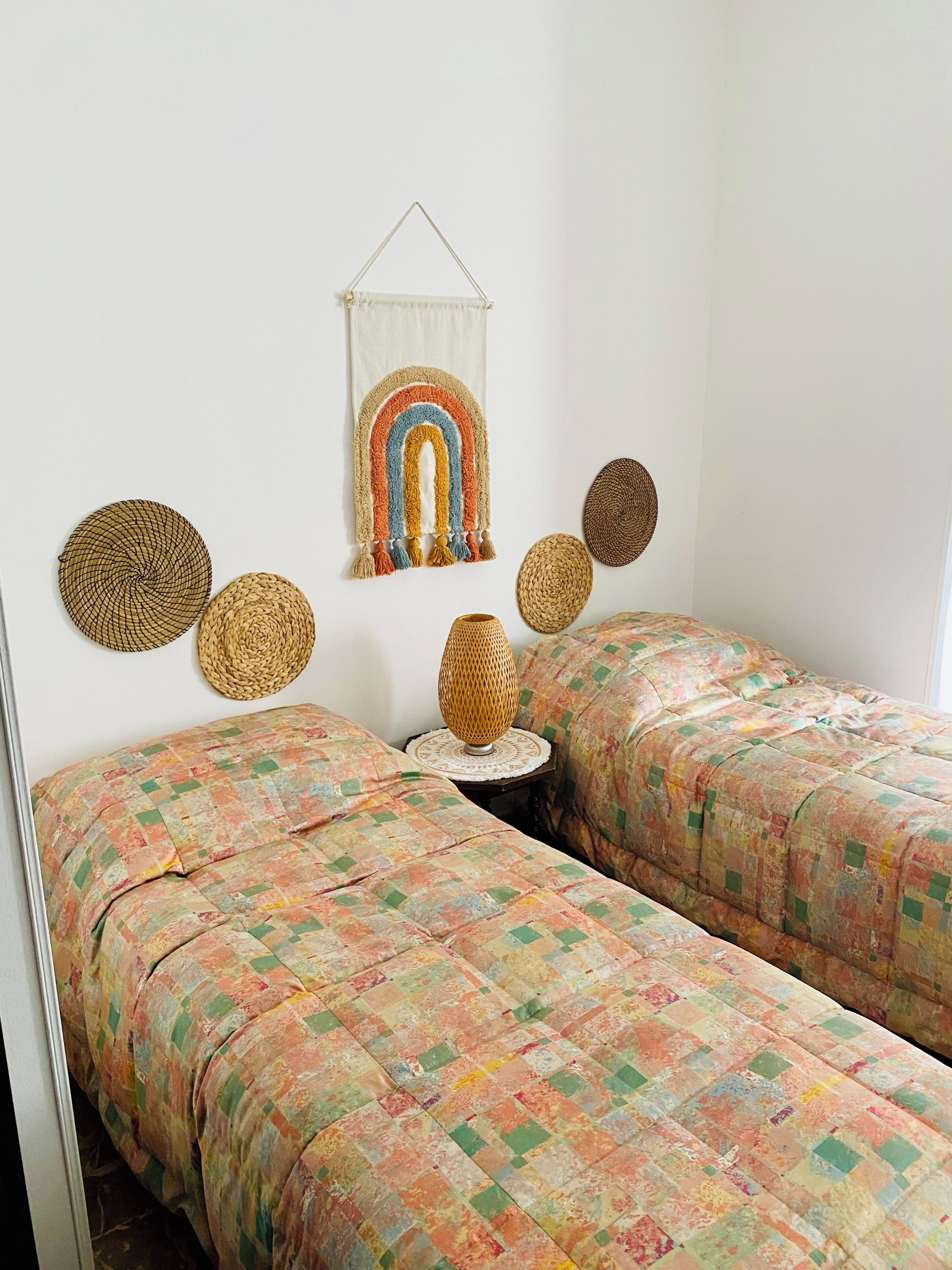 Ein Zimmer mit zwei Betten, einer Wanddekoration und einer gewobenen Lampe.