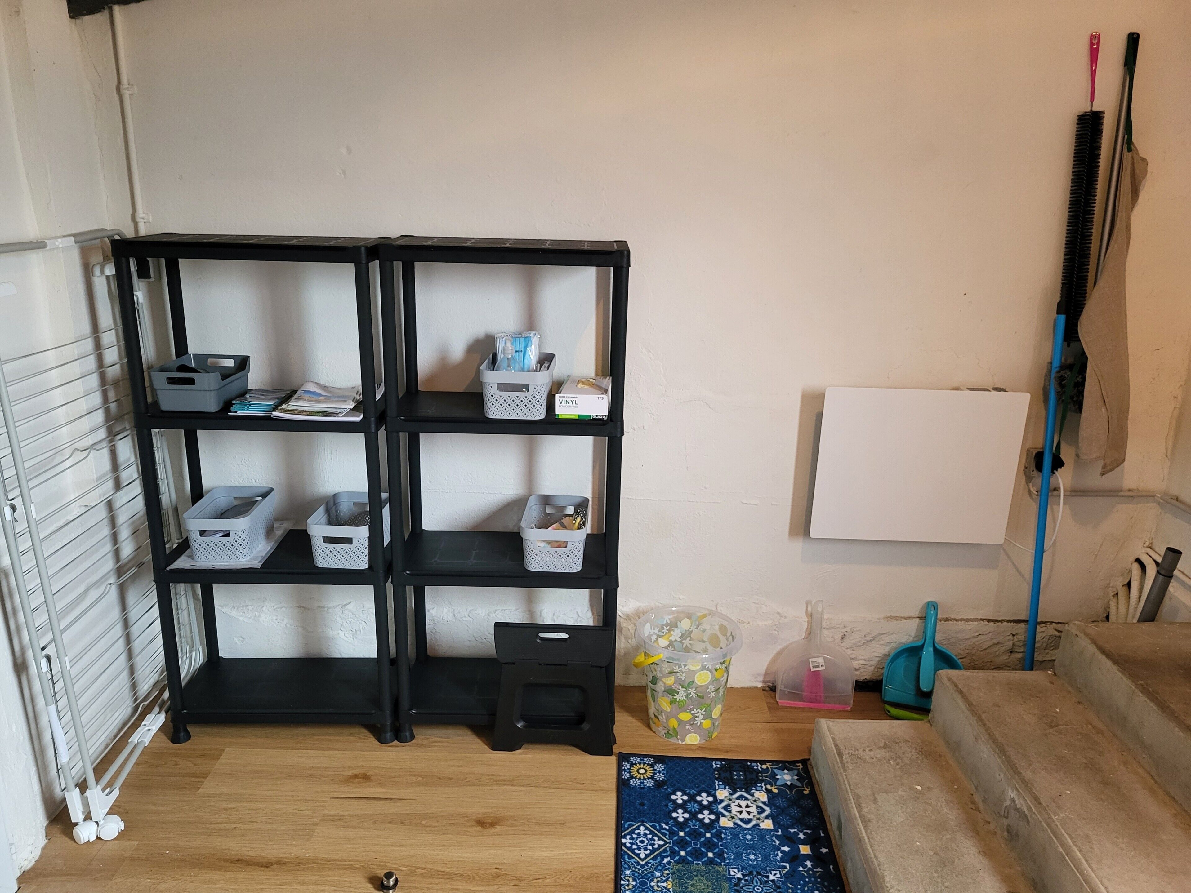 Une pièce avec une étagère noire contenant des paniers de rangement, un tableau blanc et un tapis bleu à motifs.