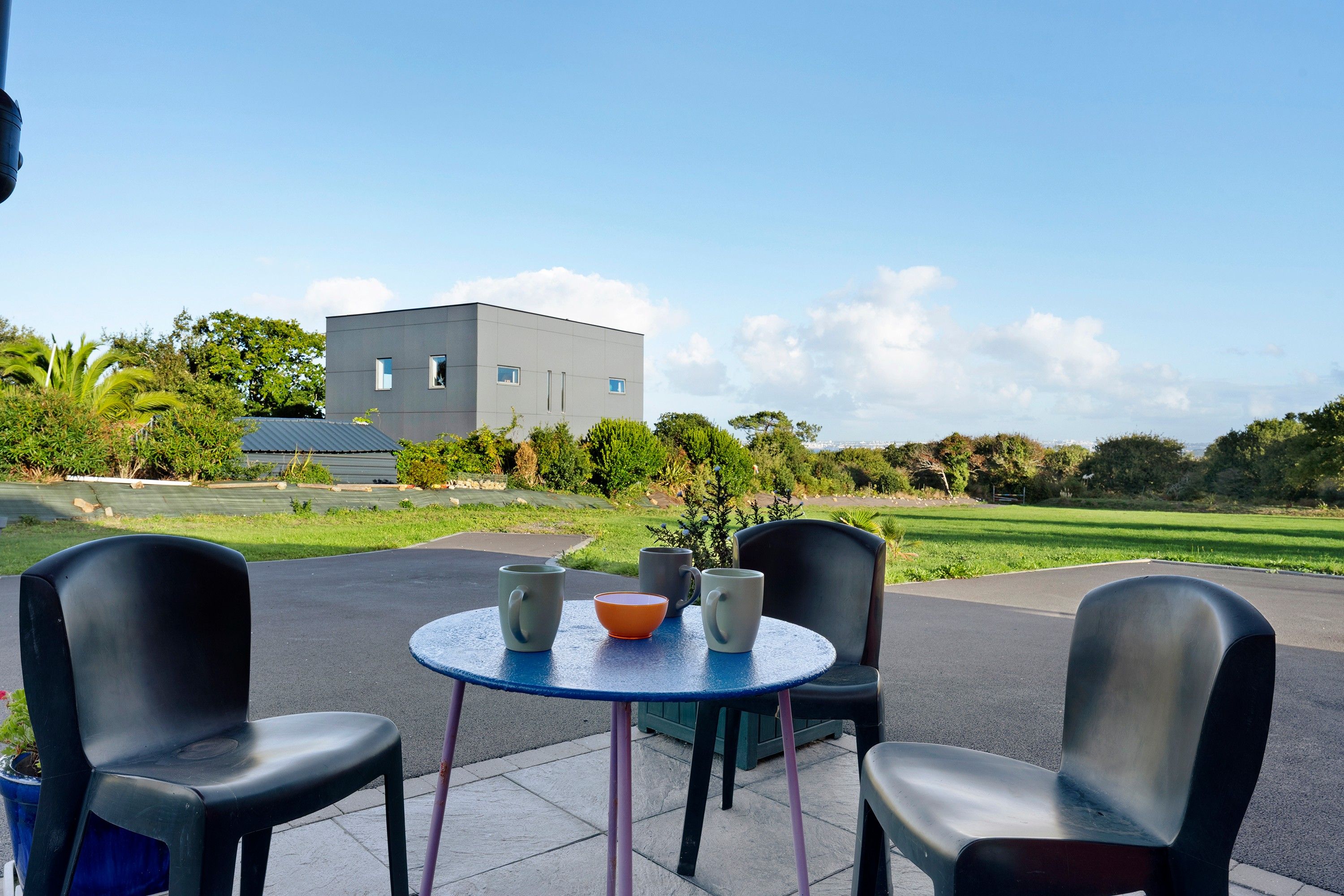 Een terras met twee tafels en vier stoelen, met een modern gebouw op de achtergrond en een heldere lucht.