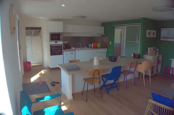 A compact kitchen with white cabinets, a built-in oven, and a microwave. There is a dining area with a table and chairs, and a small island with a sink.