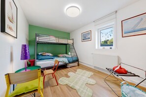 Quarto com beliches, uma escrivaninha com cadeira, janela com vista e radiador.