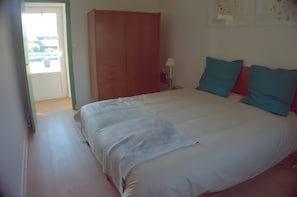 A bedroom with a bed, a wardrobe, a nightstand, and a wall with a bulletin board.