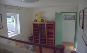 A room with a wooden wardrobe, a yellow toy bicycle, and a window with a view of the outside.