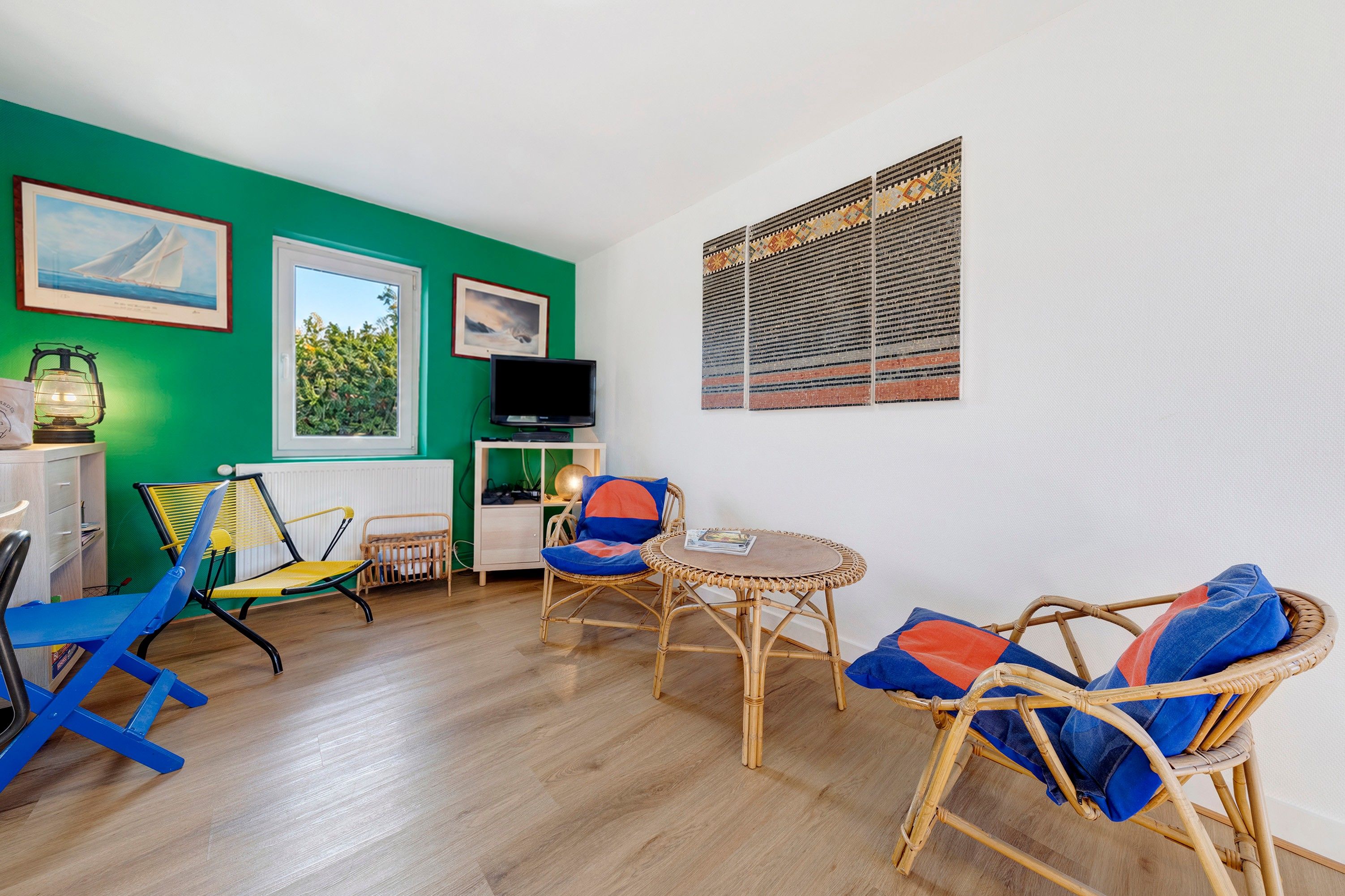 Una habitación con paredes verdes, un televisor, muebles de mimbre y cuadros enmarcados.