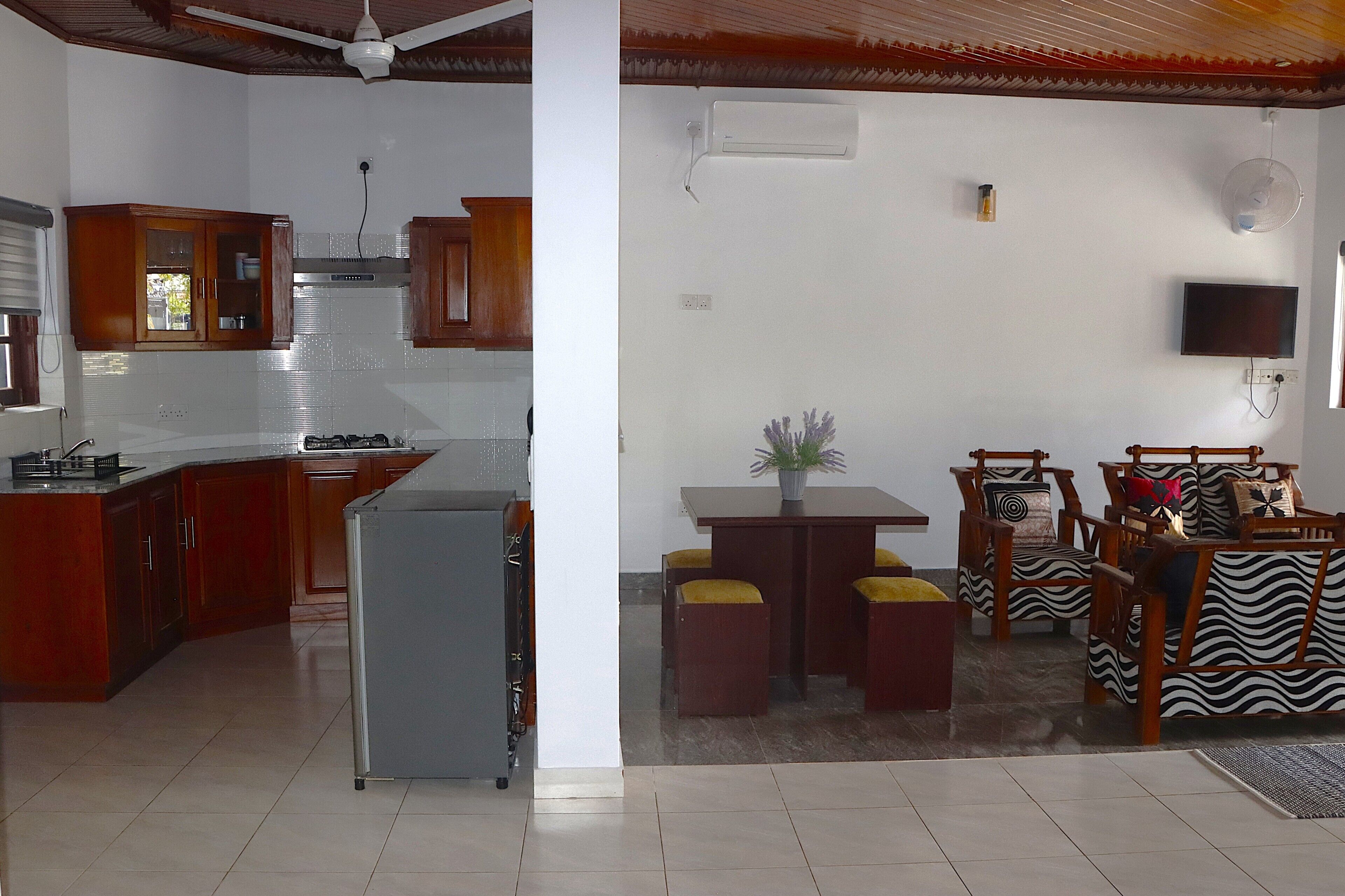 A kitchen with wooden cabinets, a refrigerator, and a dining area with a table and chairs.
