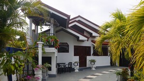 A modern two-story house with a balcony, potted plants, and a tiled walkway.
