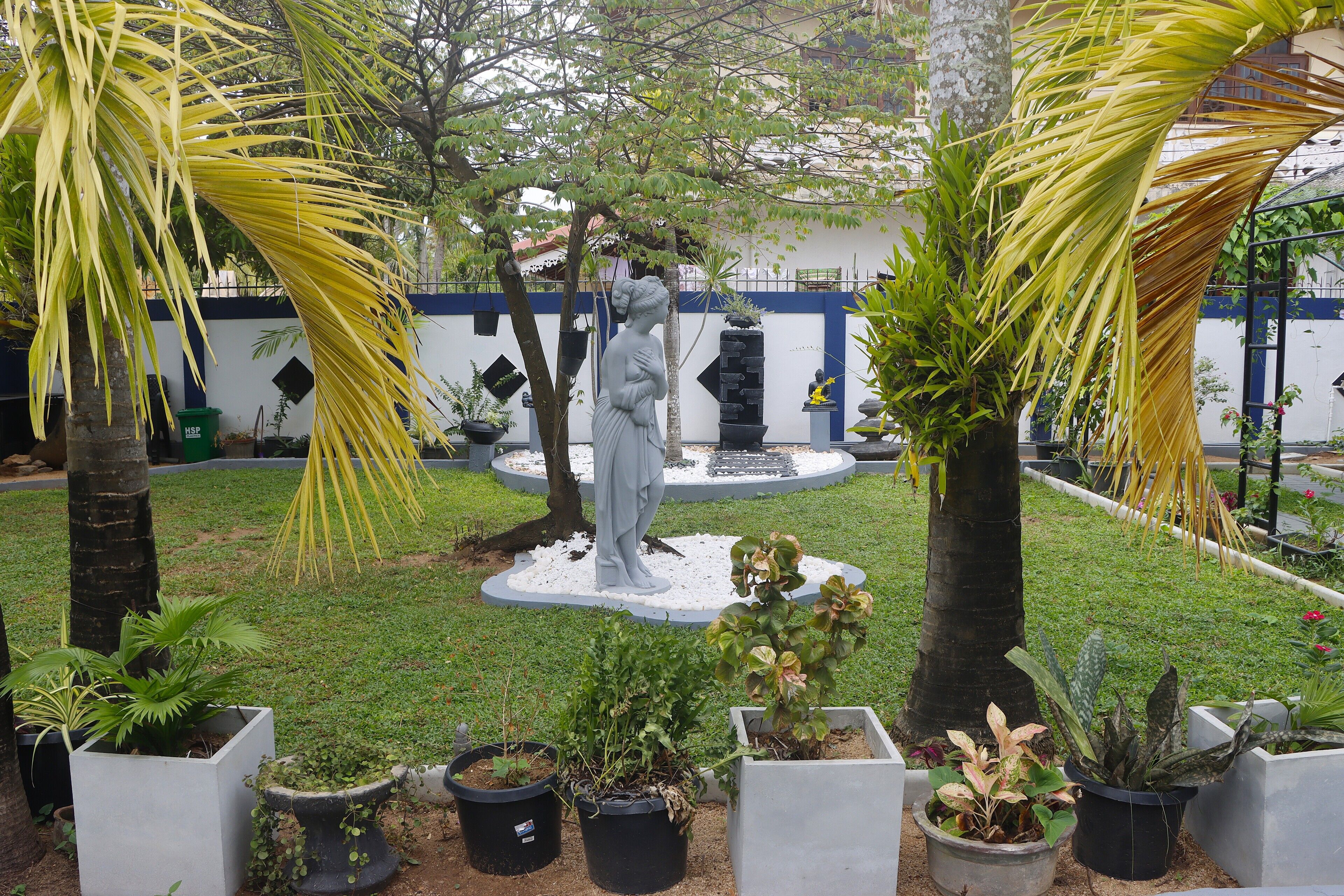 A garden with a statue, palm trees, and potted plants.
