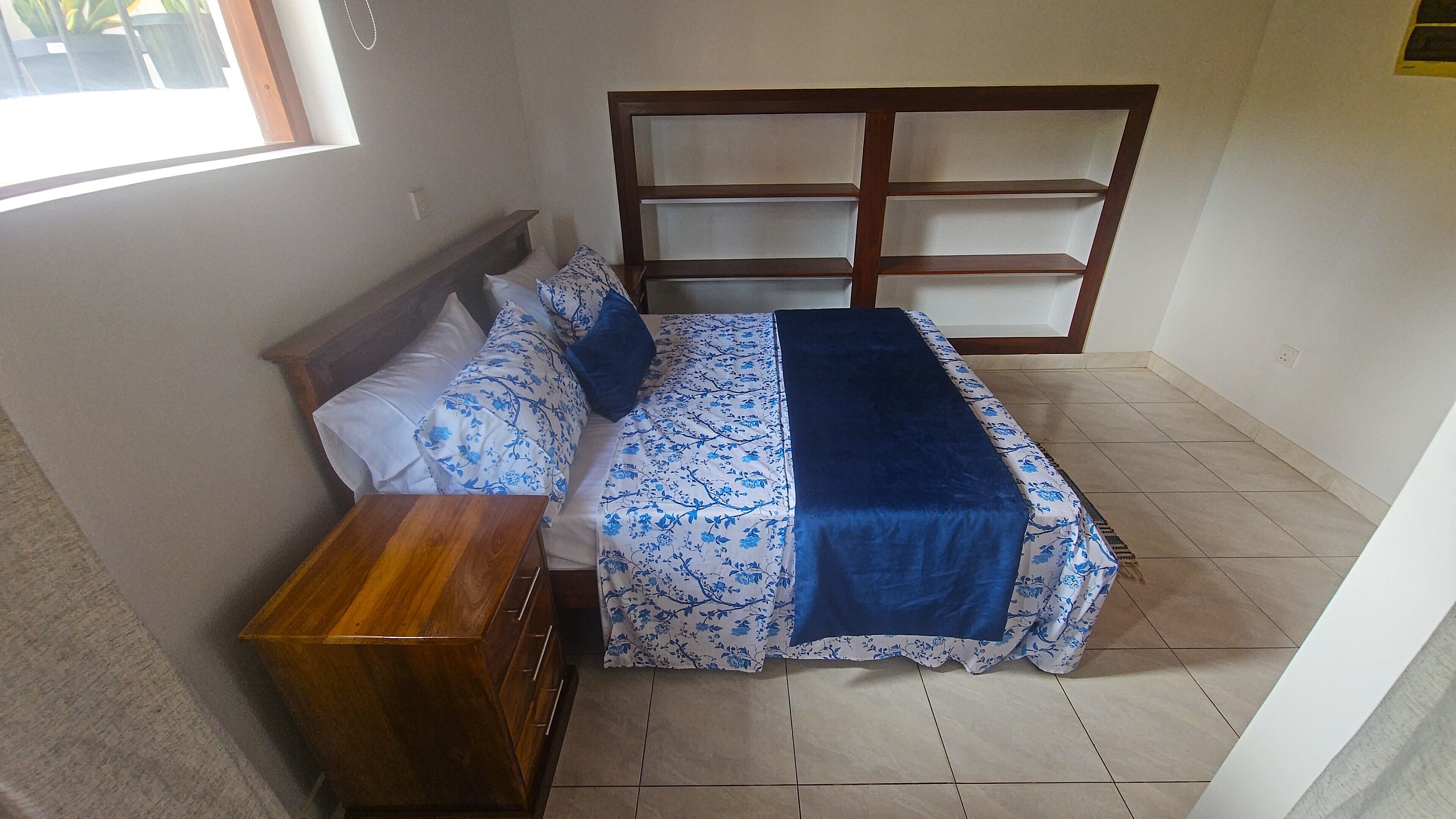 A bedroom with a bed, a wooden nightstand, and a window.